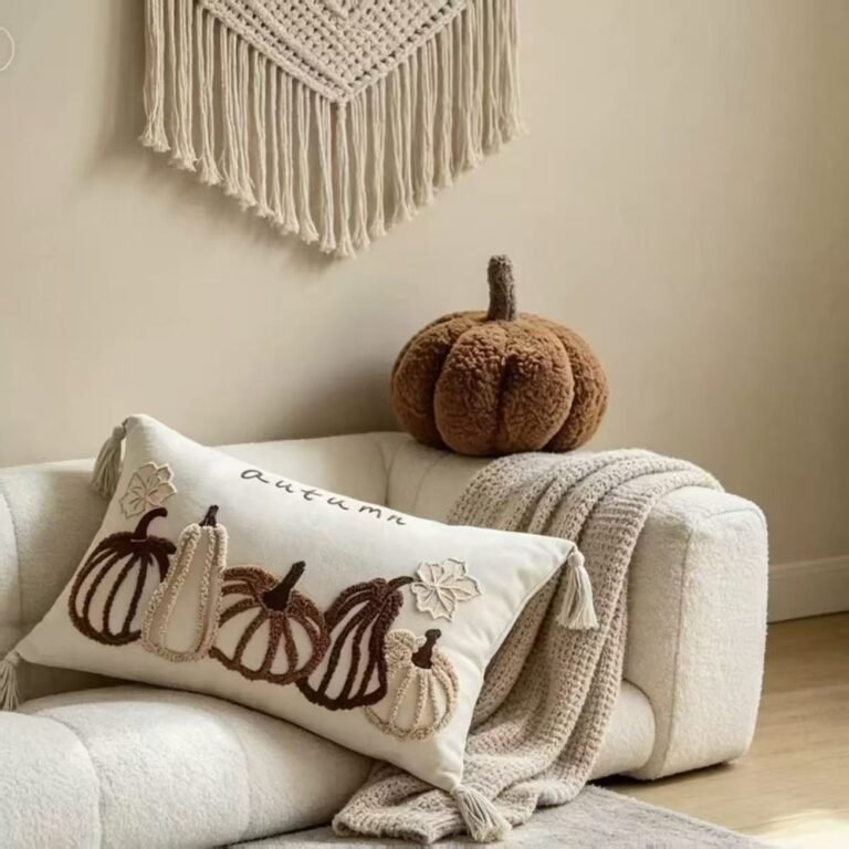 Pumpkin-pattern cushion, knitted throw and decorative pumpkin on a cream sofa