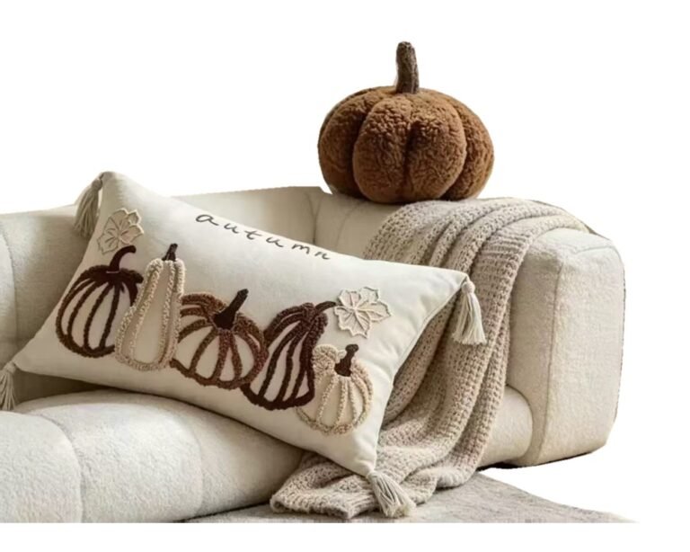 Pumpkin-pattern cushion, knitted throw and pumpkin-shaped cushion on a cream sofa against a white background