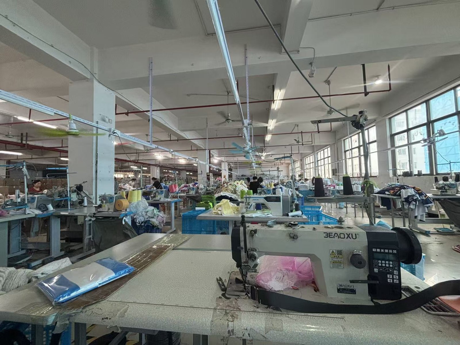 Textile factory with rows of sewing machines, workers and fabric workstations