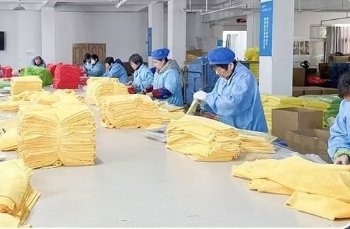 Workers in blue uniforms inspecting and stacking yellow towels in a textile workshop